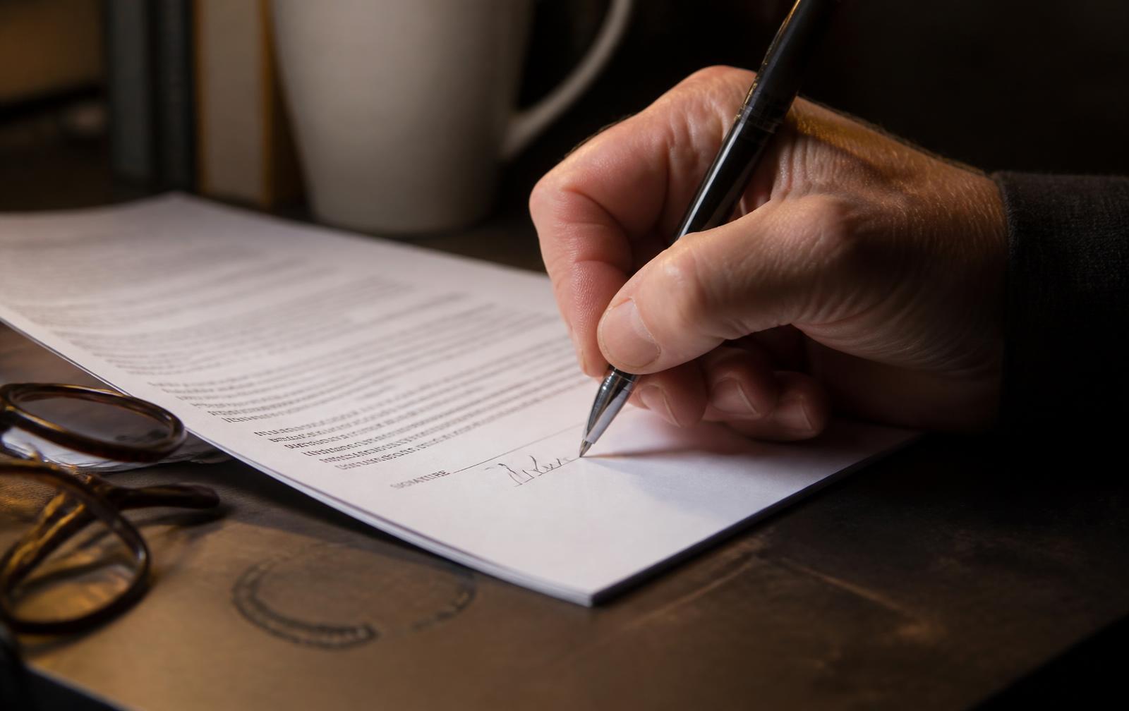 Executive signing a representation contract on a dark desk